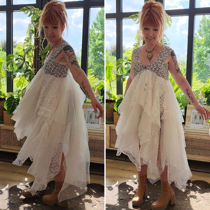 May include: A white lace dress with a high-low hemline and a patterned bodice. The dress features layered ruffles and a split front, creating a flowing silhouette. The model is wearing brown platform boots.