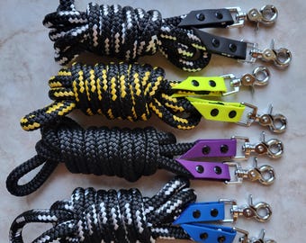 May include: Four black and white rope leashes with different colored leather handles and silver clips. The leashes are black with white stripes, black with yellow stripes, black, and black with white stripes. The handles are black with green, purple, blue, and yellow accents.