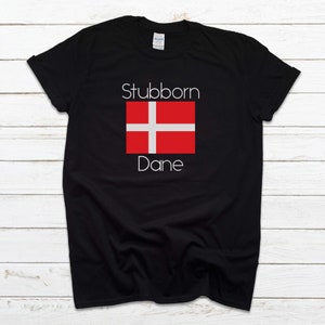May include: Black t-shirt with white text that reads "Stubborn Dane" and a red and white Danish flag.
