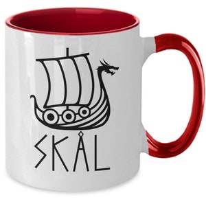 May include: White ceramic mug with a red rim and handle. The mug features a black and white illustration of a Viking ship with a dragon head and the word "SKAL" in black.