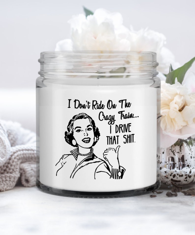May include: White candle jar with a black and white illustration of a woman with the text "I Don't Ride On The Crazy Train... I Drive That Shit."