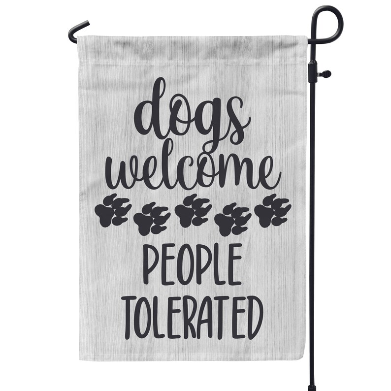 May include: A white garden flag with a woodgrain pattern and black text that reads "dogs welcome people tolerated" with five black paw prints below the text.