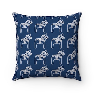 Puede incluir: Una almohada azul marino con un patr&oacute;n blanco repetido de caballos estilizados.