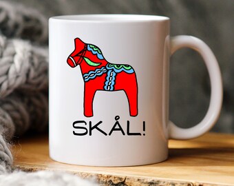 May include: White ceramic mug with a red, blue, and green Dala horse illustration and the text "SKÅL!" printed on it.