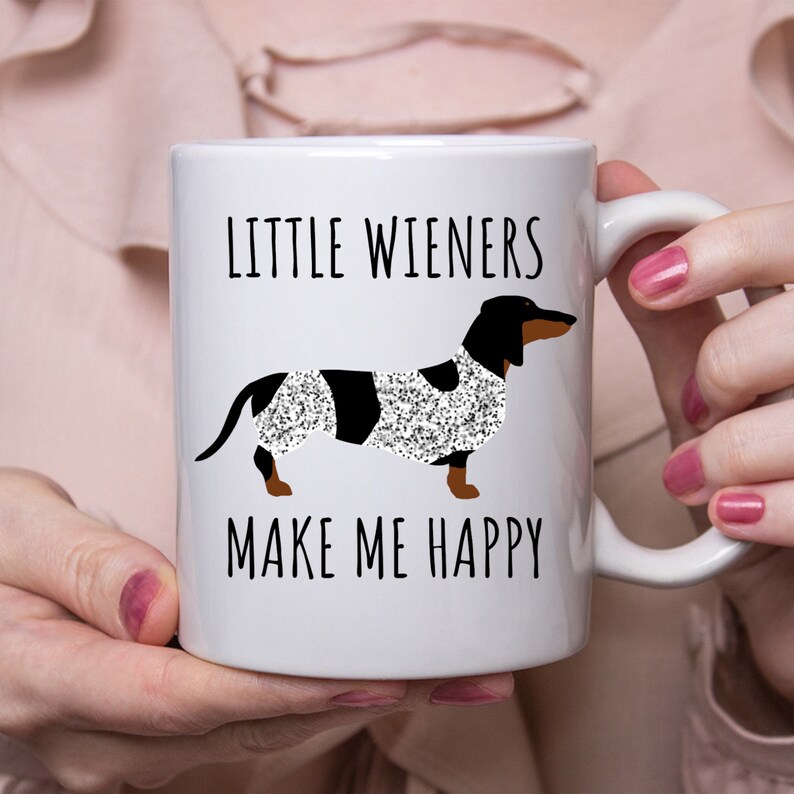 K&ouml;nnte beinhalten: Wei&szlig;e Keramik-Kaffeetasse mit einem schwarzen Dackel, der einen glitzernden wei&szlig;en und schwarzen Mantel tr&auml;gt. Die Tasse tr&auml;gt die Aufschrift "Little Wieners Make Me Happy."