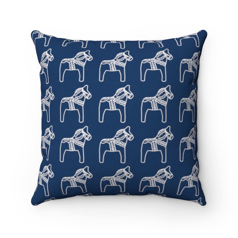Puede incluir: Una almohada azul marino con un patr&oacute;n blanco de caballos Dala suecos repetidos.