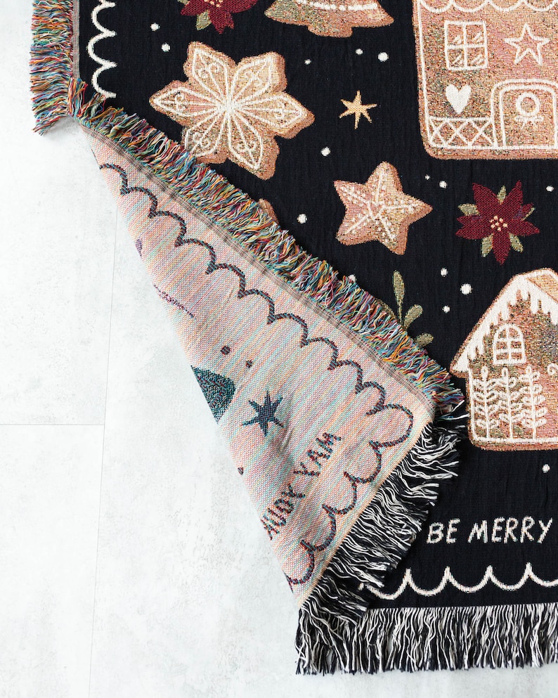 K&ouml;nnte beinhalten: Eine schwarze gewebte Wolldecke mit Weihnachtsmotiv. Die Decke zeigt Lebkuchenh&auml;user, Sterne und den Text "Be Merry".