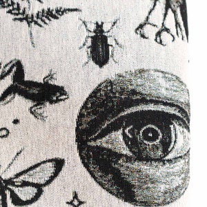 May include: A woven textile fabric featuring a black and white pattern of a large human eye, a beetle, a frog, a moth, and fern leaves. The design is rendered in a high-contrast monochrome style with intricate details on each of the natural elements.