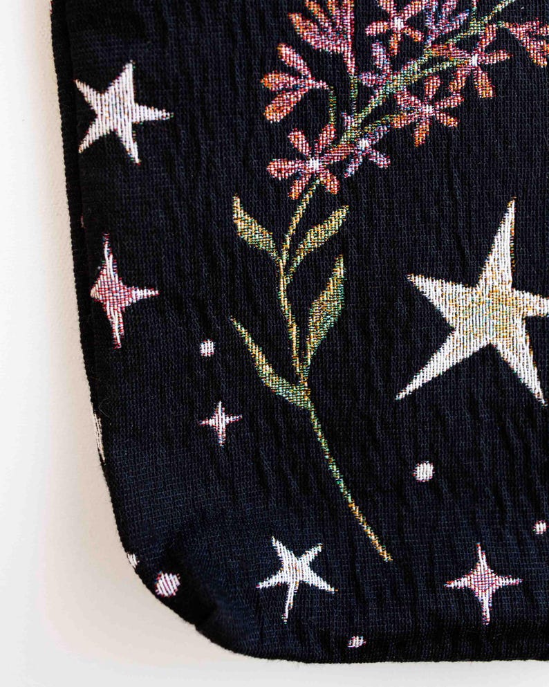 May include: Black fabric with a floral and star pattern. The fabric has a textured, woven look. The flowers are pink, purple, and green. The stars are white and silver.