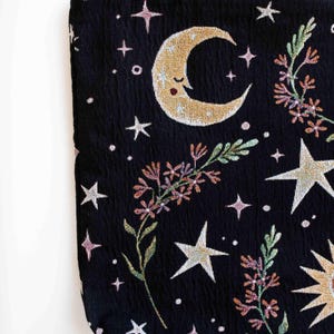May include: Black tote bag with a moon, stars, and floral design. The moon has a smiling face and the stars are white. The flowers are pink, green, and orange.