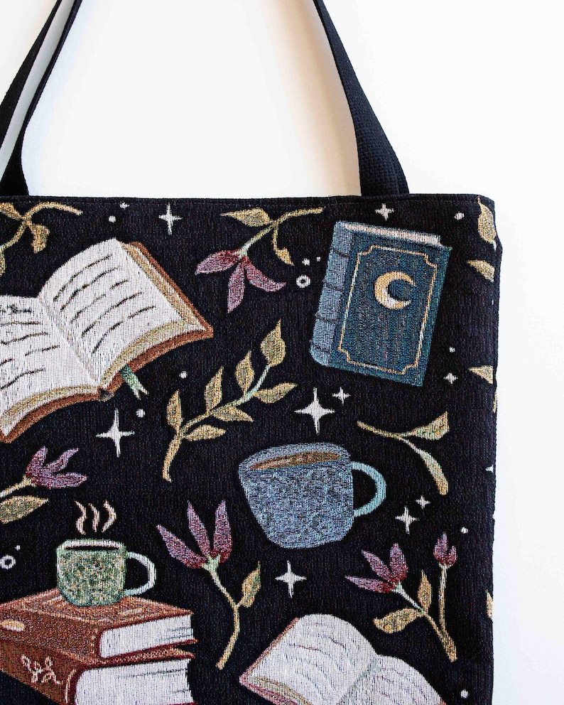 May include: Black tote bag with a tapestry design featuring books, coffee cups, stars, and leaves. The bag has a black strap.