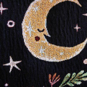 May include: A black fabric with a gold crescent moon with a sleeping face, a white star, and a floral design in the bottom right corner.