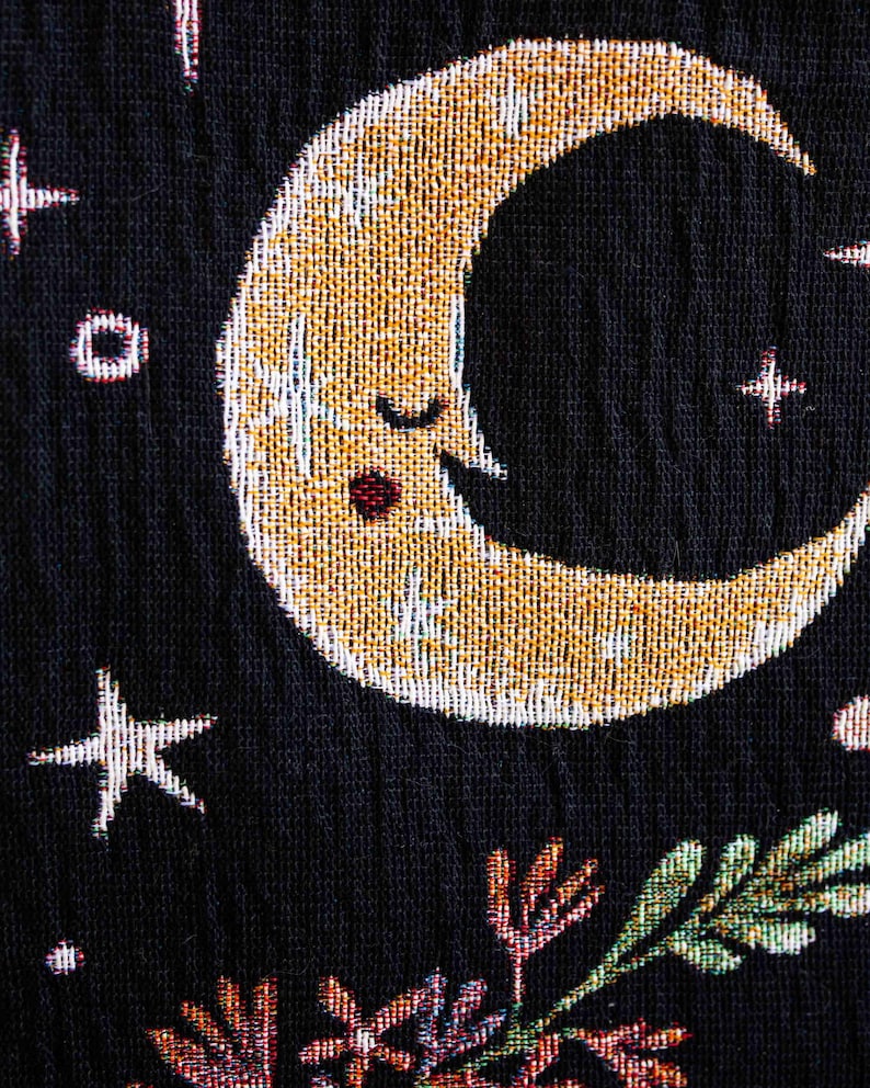 May include: A black fabric with a gold crescent moon with a sleeping face, a white star, and a floral design in the bottom right corner.