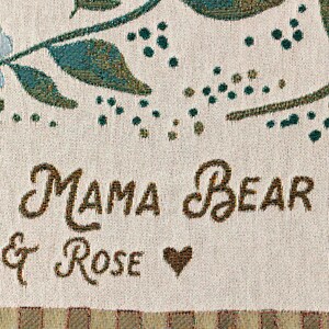 May include: A white woven throw blanket with a brown and green floral design and the text "Mama Bear & Rose" with a heart.