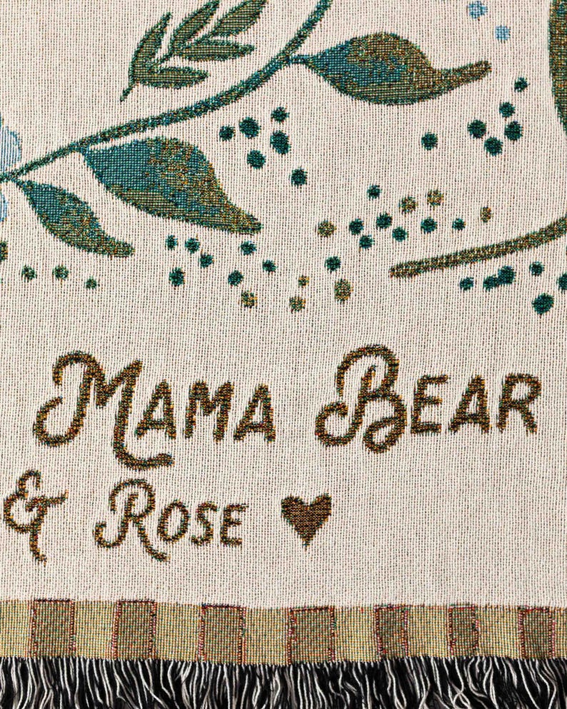 May include: A white woven throw blanket with a brown and green floral design and the text "Mama Bear & Rose" with a heart.
