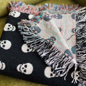 May include: Black throw blanket with a white skull pattern. The blanket has fringe on all sides.