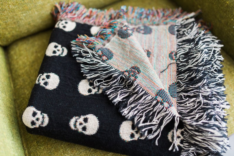 May include: Black throw blanket with a white skull pattern. The blanket has fringe on all sides.