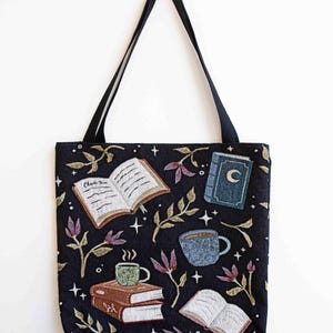 May include: Black tote bag with a whimsical design featuring books, coffee cups, and stars. The text "Chapter One" is visible on one of the books.