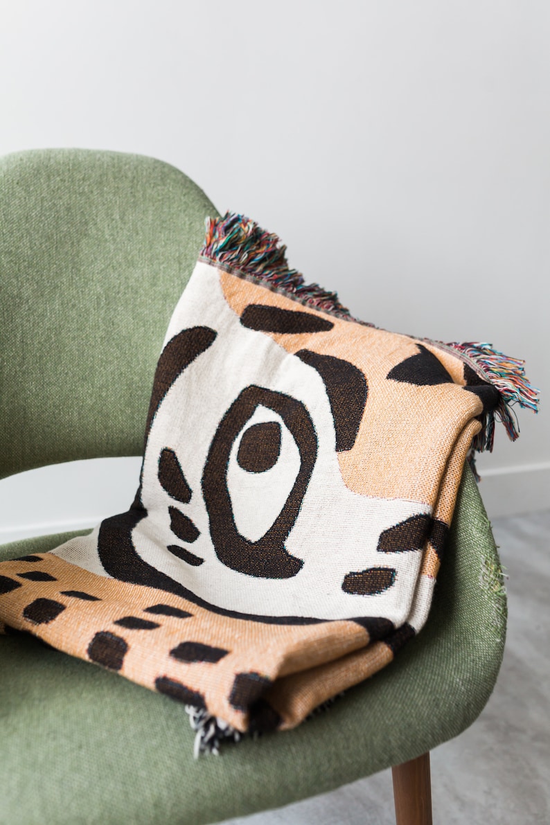 May include: A green armchair with a woven throw blanket featuring a geometric pattern in shades of brown, beige, and white. The blanket has fringed edges.