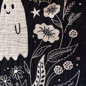 May include: Black fabric with a white embroidered design of a ghost, flowers, stars, and leaves. The ghost has a smiling face and a simple body shape.