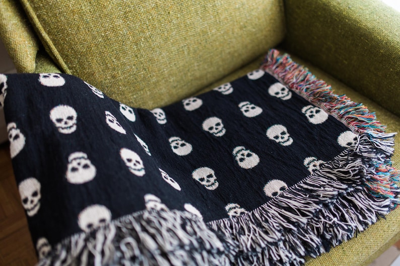 May include: Black and white throw blanket with a skull pattern and fringe. The blanket is draped over a green armchair.