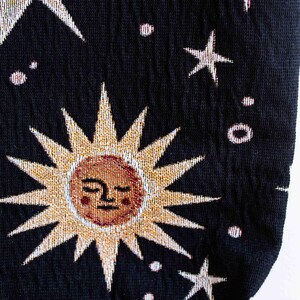 May include: Black fabric tote bag with a tapestry design of a sun with a face, stars, and small white dots.