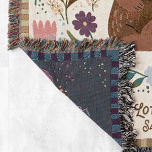 May include: A woven throw blanket featuring a floral design and a brown bear. The blanket has a fringed edge and the text "Lots of love" is visible in the bottom right corner.