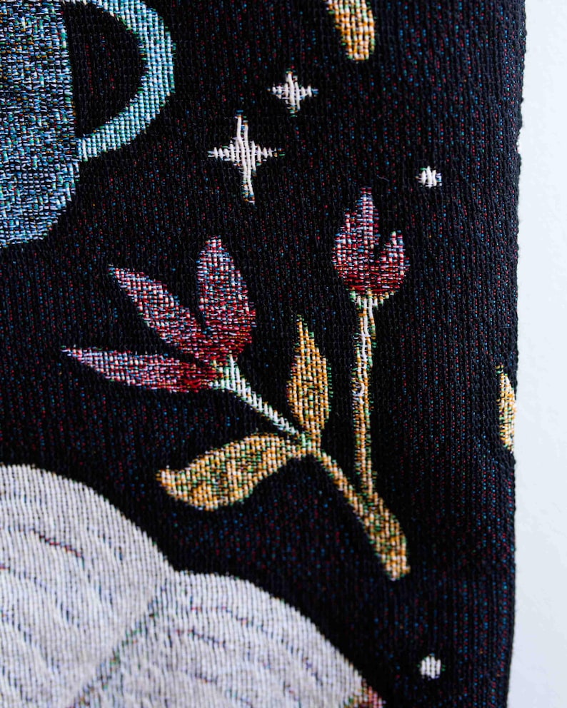 May include: A black tapestry with a white floral design and a blue crescent moon. The tapestry has a textured woven fabric.