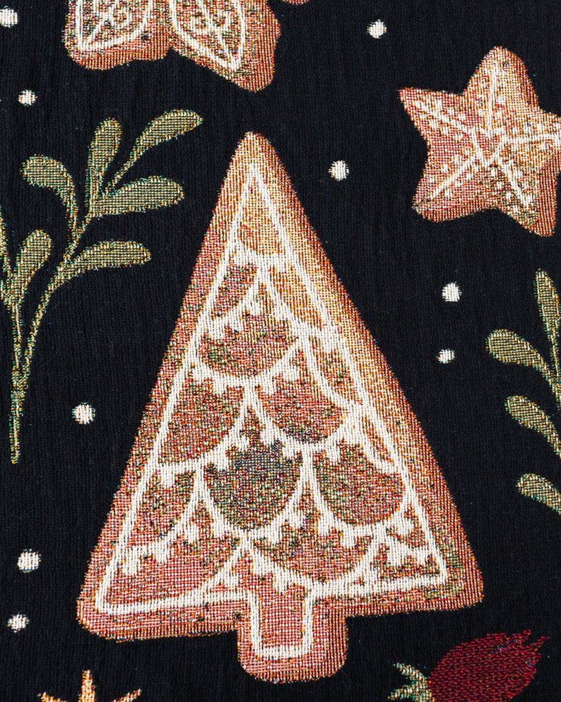 K&ouml;nnte beinhalten: Nahaufnahme eines braunen und wei&szlig;en Weihnachtsbaum-Designs auf einem schwarzen Stoffhintergrund. Der Baum ist mit einem goldenen und wei&szlig;en Muster verziert.