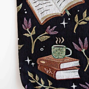 May include: Black tapestry tote bag with a whimsical design featuring a book, a cup of coffee, and floral elements. The book has the text "Chapter One" written on it.