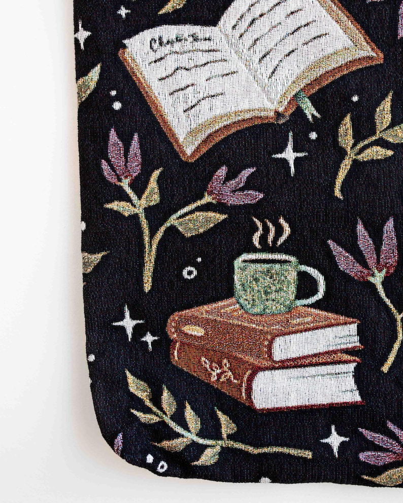 May include: Black tapestry tote bag with a whimsical design featuring a book, a cup of coffee, and floral elements. The book has the text "Chapter One" written on it.