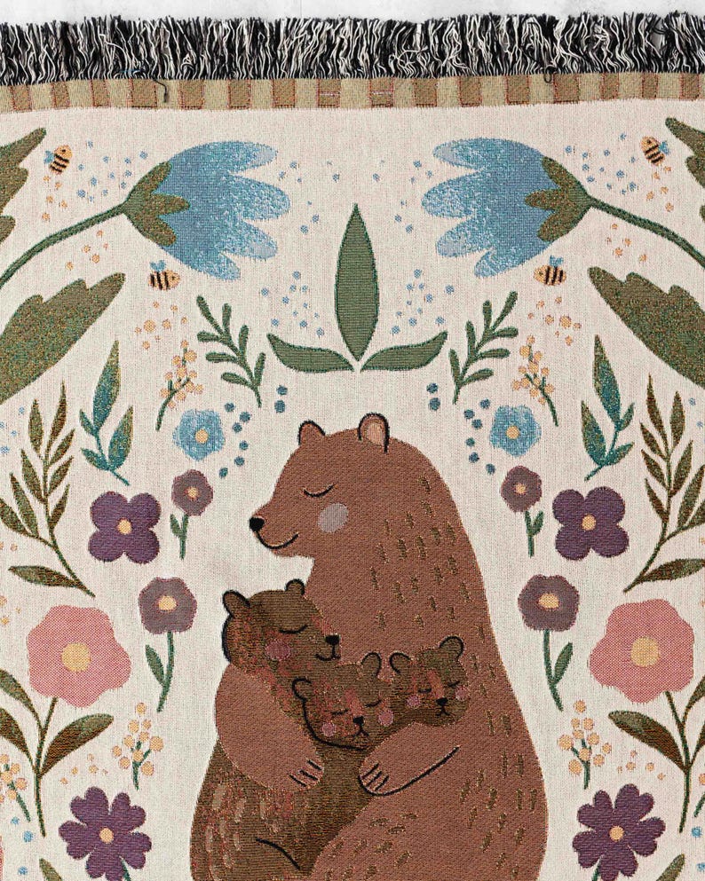 May include: A woven tapestry depicting a brown bear mother cuddling her two cubs. The background is cream with a floral design in shades of pink, purple, blue, and green.