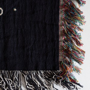 May include: Black woven throw blanket with a colourful fringe border and a white fringe on the bottom edge.