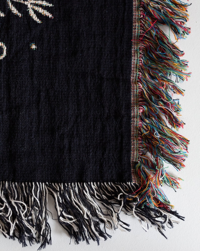 May include: Black woven throw blanket with a colourful fringe border and a white fringe on the bottom edge.