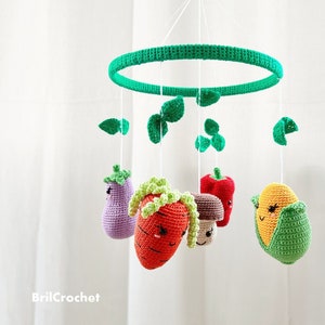 May include: A green crocheted mobile with a variety of crocheted vegetables hanging from it. The vegetables include a carrot, eggplant, corn, mushroom, and a red pepper.