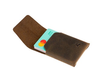 May include: A brown leather card holder with a flap that opens to reveal a stack of credit cards. The card holder has a distressed look and a small logo on the front.