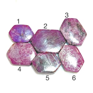 May include: Six hexagonal gemstones in shades of pink and purple are displayed. The polished stones have a marbled appearance with varying patterns and textures. These gemstones are likely used for jewellery making or collecting. Each stone is approximately 2-3 cm in diameter.