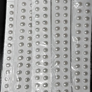 May include: Several blister packs of white, round pearls in varying sizes. Each pack contains multiple pearls arranged in rows. The packaging includes text in Chinese and English, with labels for species, size, and grade.