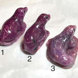 May include: Three small, polished, deep purple stone figurines shaped like seals, each with a smooth, glossy finish and dark eyes. The figurines are numbered 1, 2, and 3, and they are arranged in a row, showcasing their distinct, mottled, and crystalline texture.