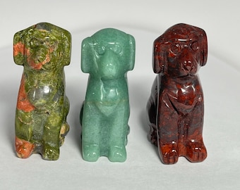 Könnte beinhalten: Drei geschnitzte Hundefiguren aus Stein in Grün-, Rot- und Brauntönen. Die Hunde sitzen aufrecht mit aufgestellten Ohren. Die Figuren sind aus poliertem Stein gefertigt und haben eine glatte, glänzende Oberfläche.