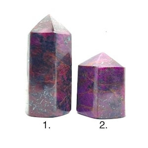 Puede incluir: Dos obeliscos de piedras preciosas pulidas. El obelisco más grande es de color magenta intenso con vetas moradas oscuras y grises. El obelisco más pequeño tiene una coloración similar. Ambos tienen una parte superior facetada y puntiaguda y una base rectangular. Numerados 1 y 2.
