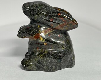 Könnte beinhalten: Eine geschnitzte Steinhasenfigur. Die Skulptur ist überwiegend dunkelgrün mit roten und gelben Flecken. Der Hase sitzt mit aufgestellten Ohren.