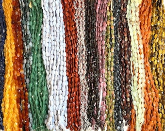 Könnte beinhalten: Eine Sammlung von Edelsteinperlen in verschiedenen Farben, darunter Blau, Orange, Grün und Rot. Die oval geformten Perlen sind aufgefädelt und bilden eine ansprechende Präsentation von Natursteinen. Das Bild zeigt eine Vielzahl von Texturen und Farbtönen.