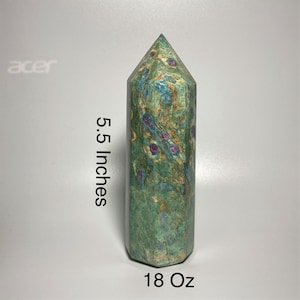 May include: A green and blue crystal obelisk with red inclusions. The obelisk is 5.5 inches tall and weighs 18 ounces. The crystal has a polished, smooth surface and a pointed top. The obelisk is a decorative item.