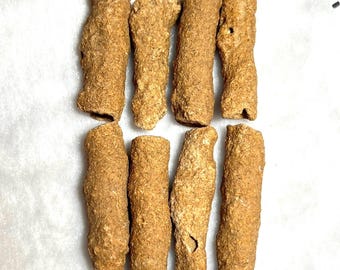 May include: Eight irregularly shaped, light brown objects are arranged in two rows of four against a white background. The objects have a rough, textured surface and vary in size and shape, resembling small, elongated pieces of natural material.