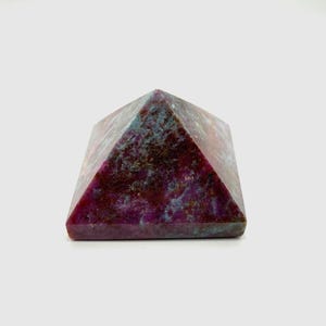 May include: A pyramid-shaped gemstone with a mix of deep red, purple, and blue hues. The stone has a textured surface and a polished finish, showcasing its natural patterns. This decorative item is ideal for home decor or as a unique gift.
