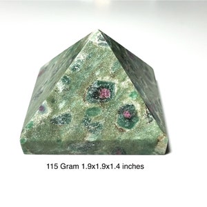 May include: A green pyramid-shaped gemstone with red and green inclusions. The pyramid is 1.9 x 1.9 x 1.4 inches and weighs 115 grams. The text on the image reads "115 Gram 1.9x1.9x1.4 inches."