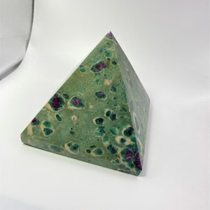 May include: A pyramid-shaped decorative object. The pyramid is green with dark green and red spots. The pyramid is made of stone and has a flat base.