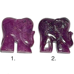 May include: Two small, carved elephant figurines in a deep magenta hue. The elephants are numbered 1 and 2, and are displayed against a white background. The carvings have visible details of the elephant's features.