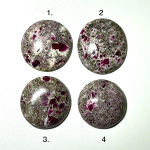 May include: Four round gemstones with a speckled gray and white base, each featuring vibrant red inclusions. The stones are numbered 1 through 4. The polished surfaces reflect light, highlighting the natural patterns and colors.